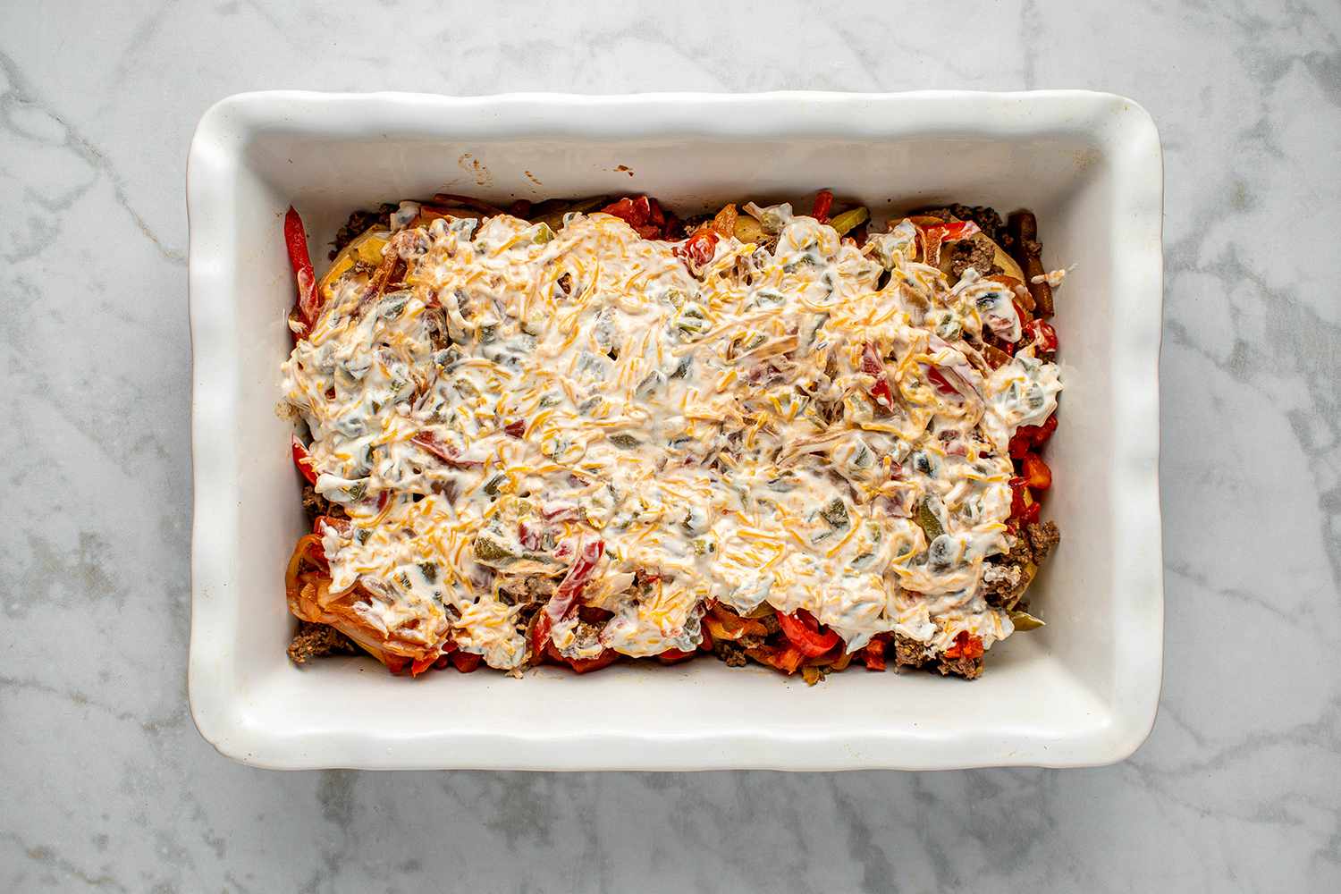 Sour cream mixture topping layered casserole in the baking dish 