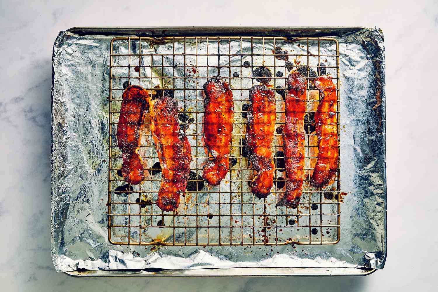 A foil-lined baking sheet with a baking rack with cooked million dollar bacon