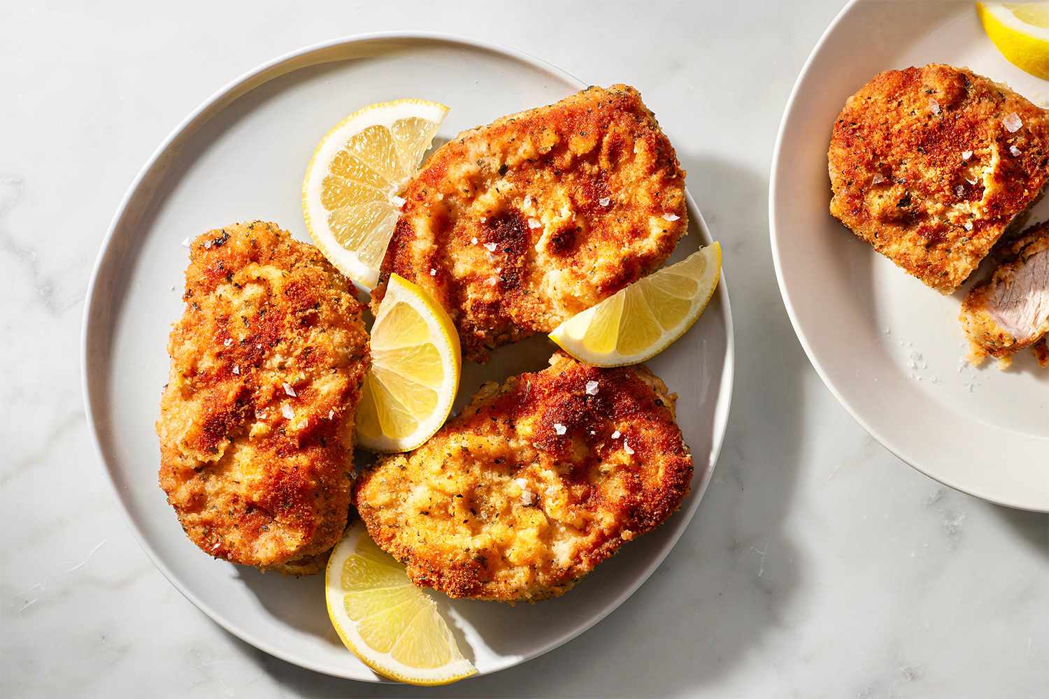 Breaded pork chops on a plate with lemon wedges 