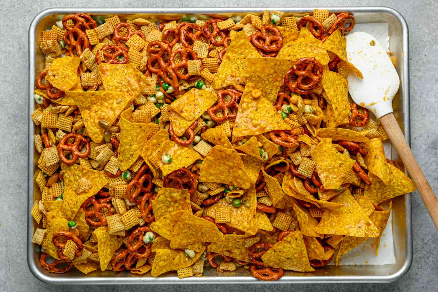 furikake chex mix being tossed with sauce on sheet pan with rubber spatula