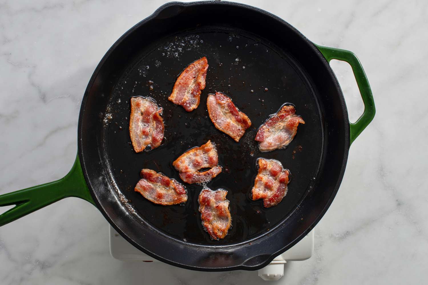Slices of bacon cooking in a cast iron skillet