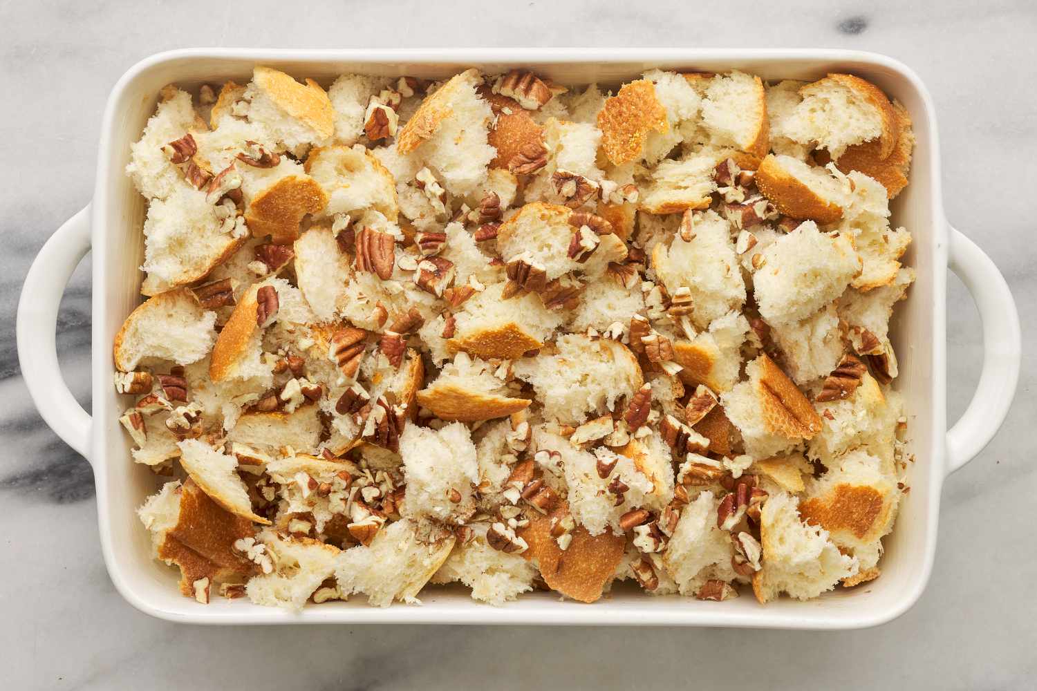 bread cubes and pecans inside of buttered casserole dish