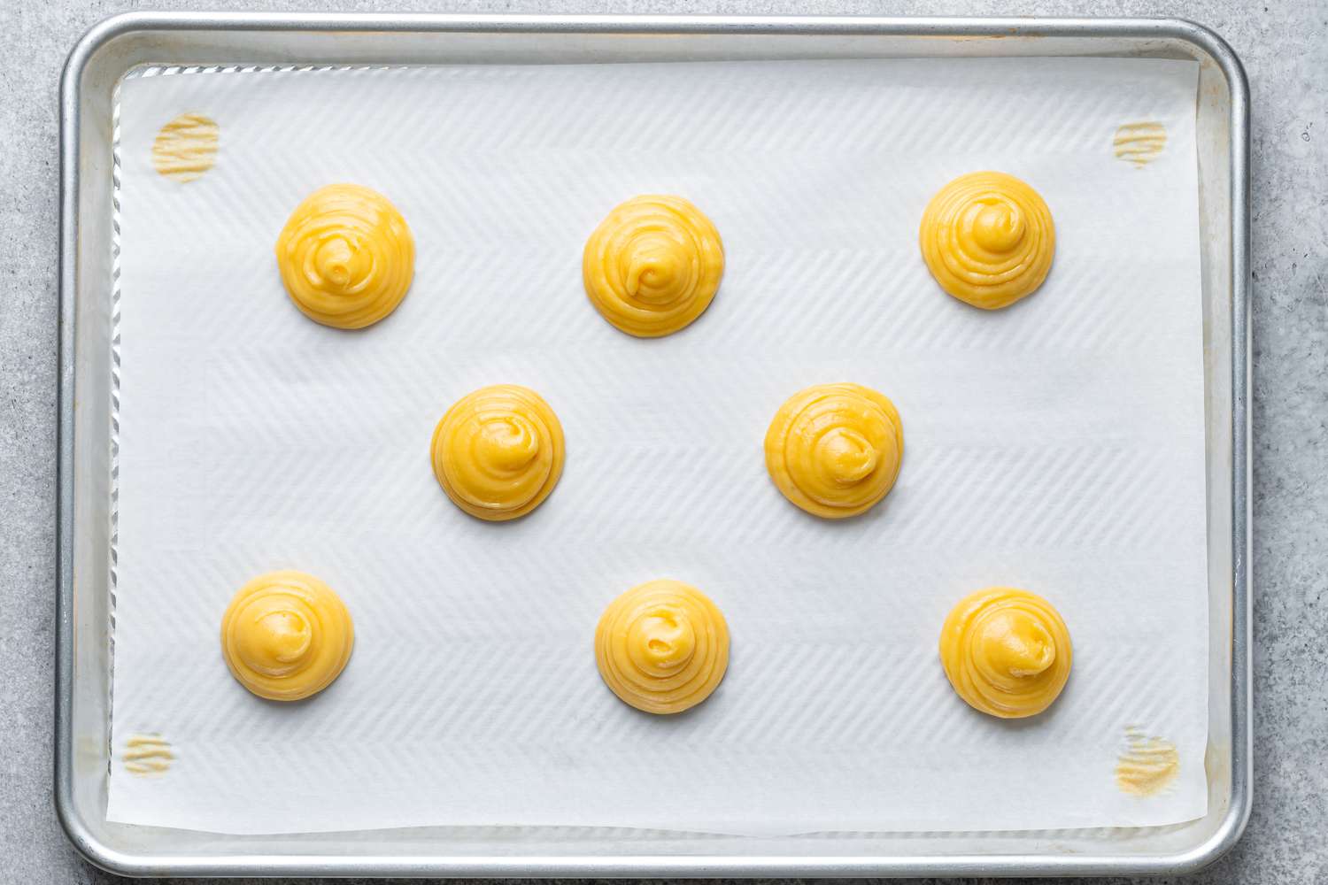 Small rounds of piped choux dough on a parchment-lined baking sheet