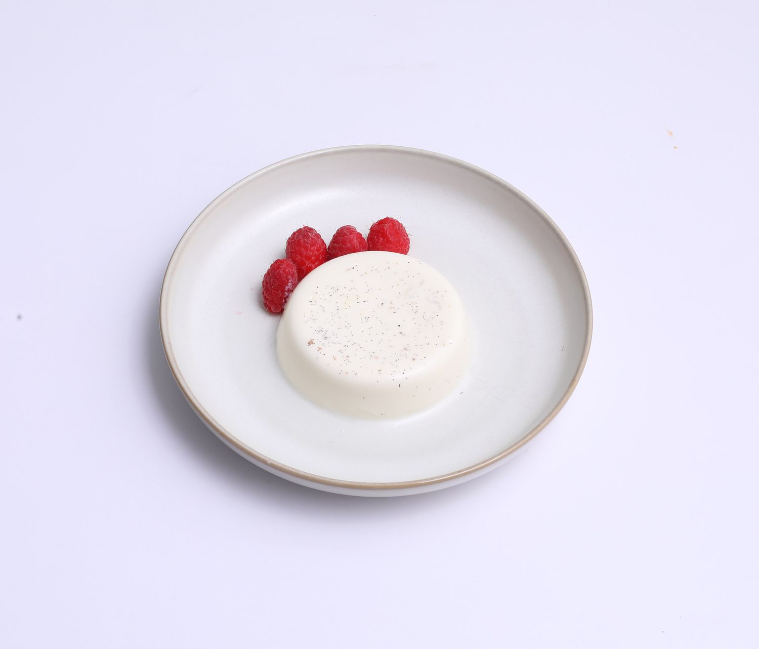 An unmolded vanilla panna cotta on a white plate with four fresh raspberries