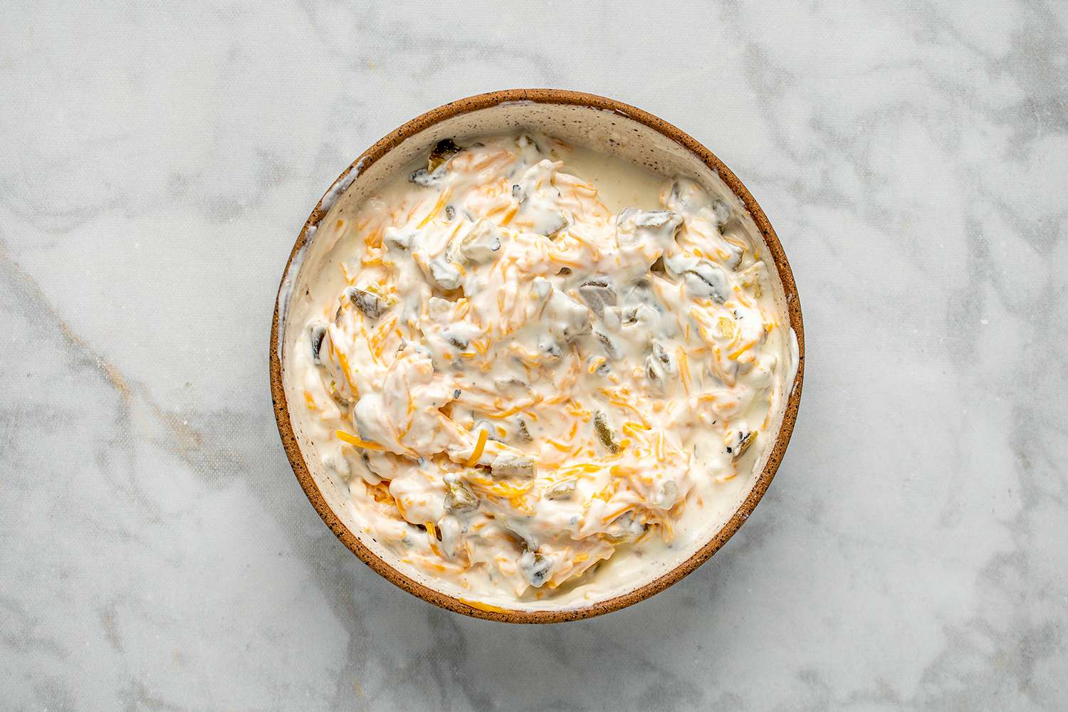 Sour cream, cheddar, and jalapeños stirred together in a bowl 