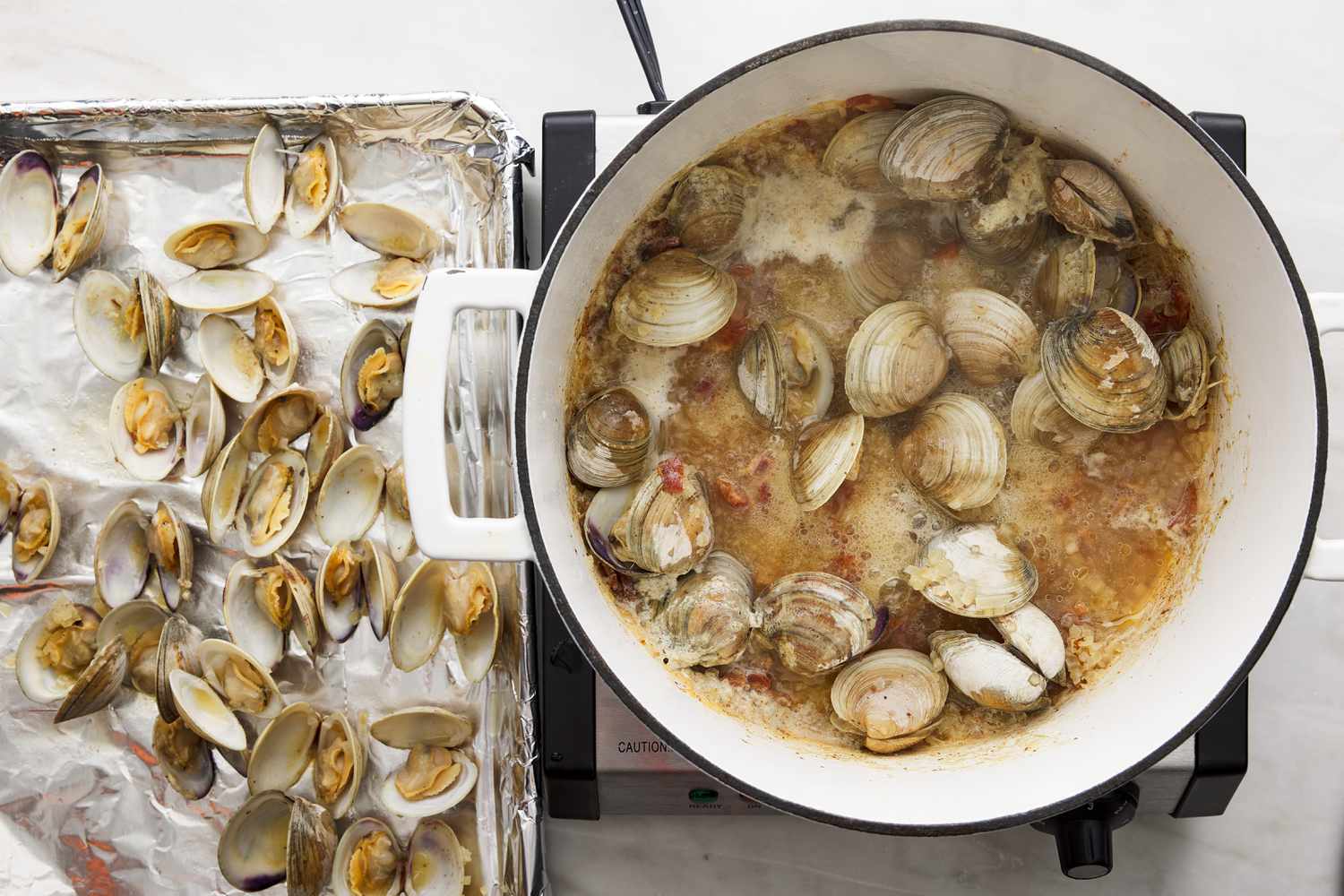 opened cooked clams on foiled lined baking sheet with pot 