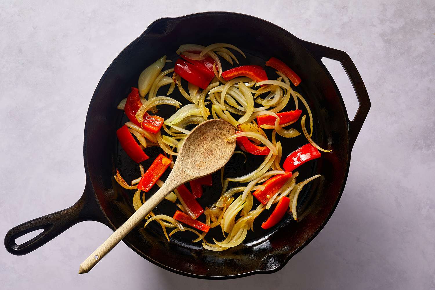 Onions and peppers in a cast iron skillet with a wooden spoon 