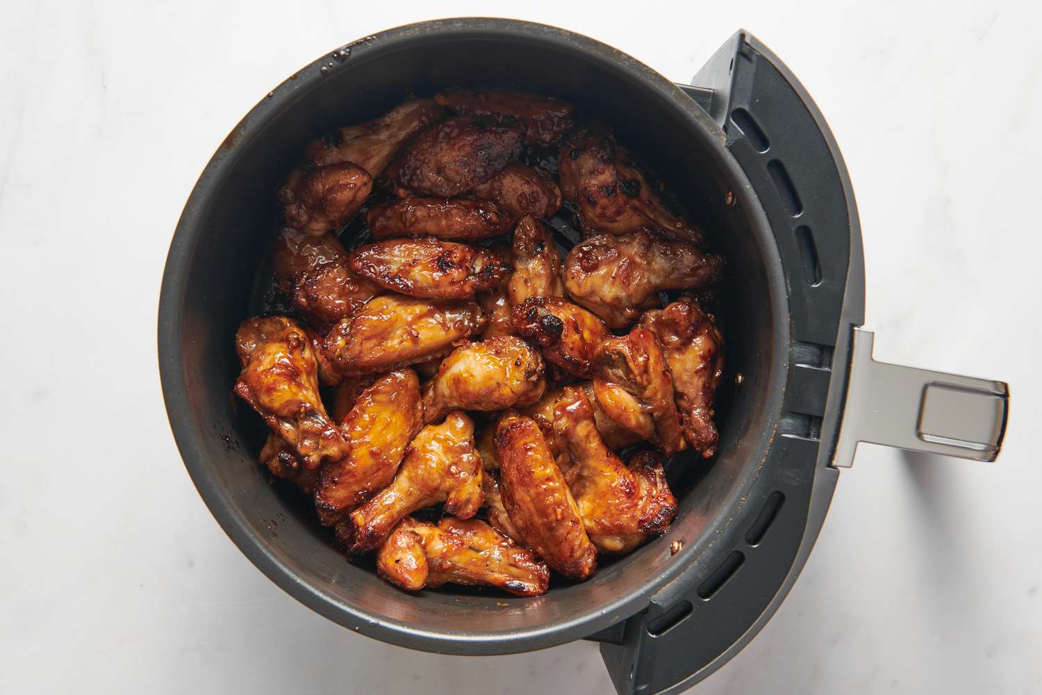 An air fryer basked with wings tossed in honey-garlic sauce