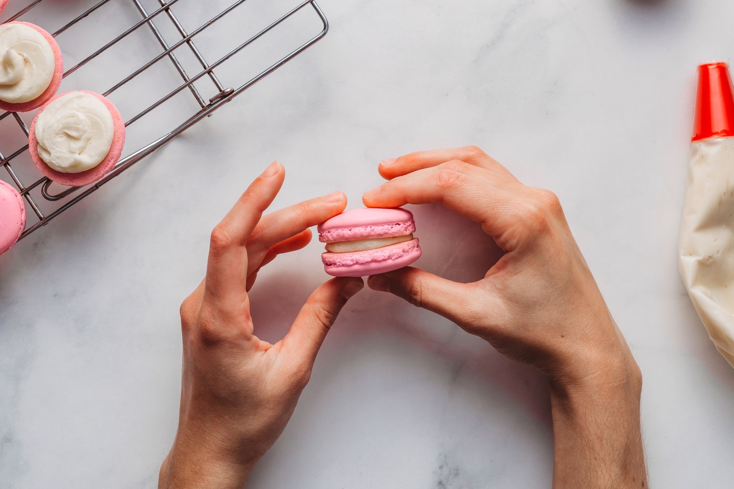 A pink macaron being held by a pair of hands