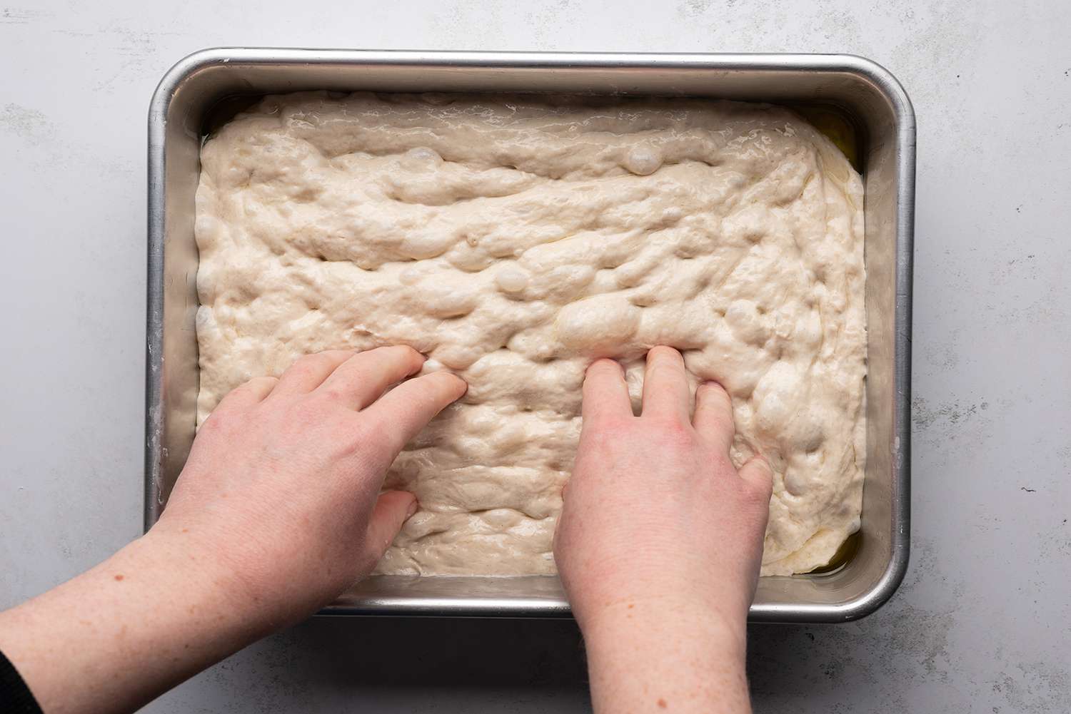 Make dimples all over the dough in the baking dish with hands