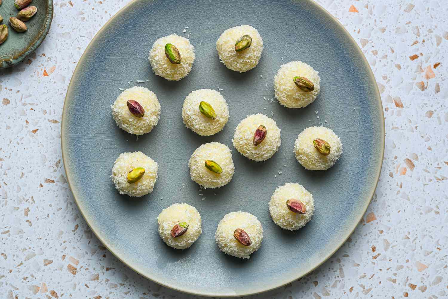 A plate of coconut laddoos, each topped with a whole, roasted pistachio