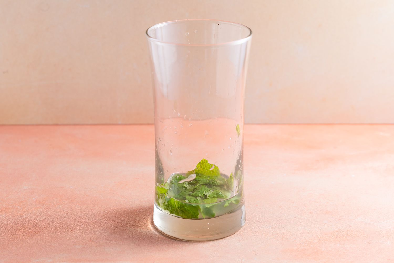 Muddled mint leaves, lime, and syrup in a glass