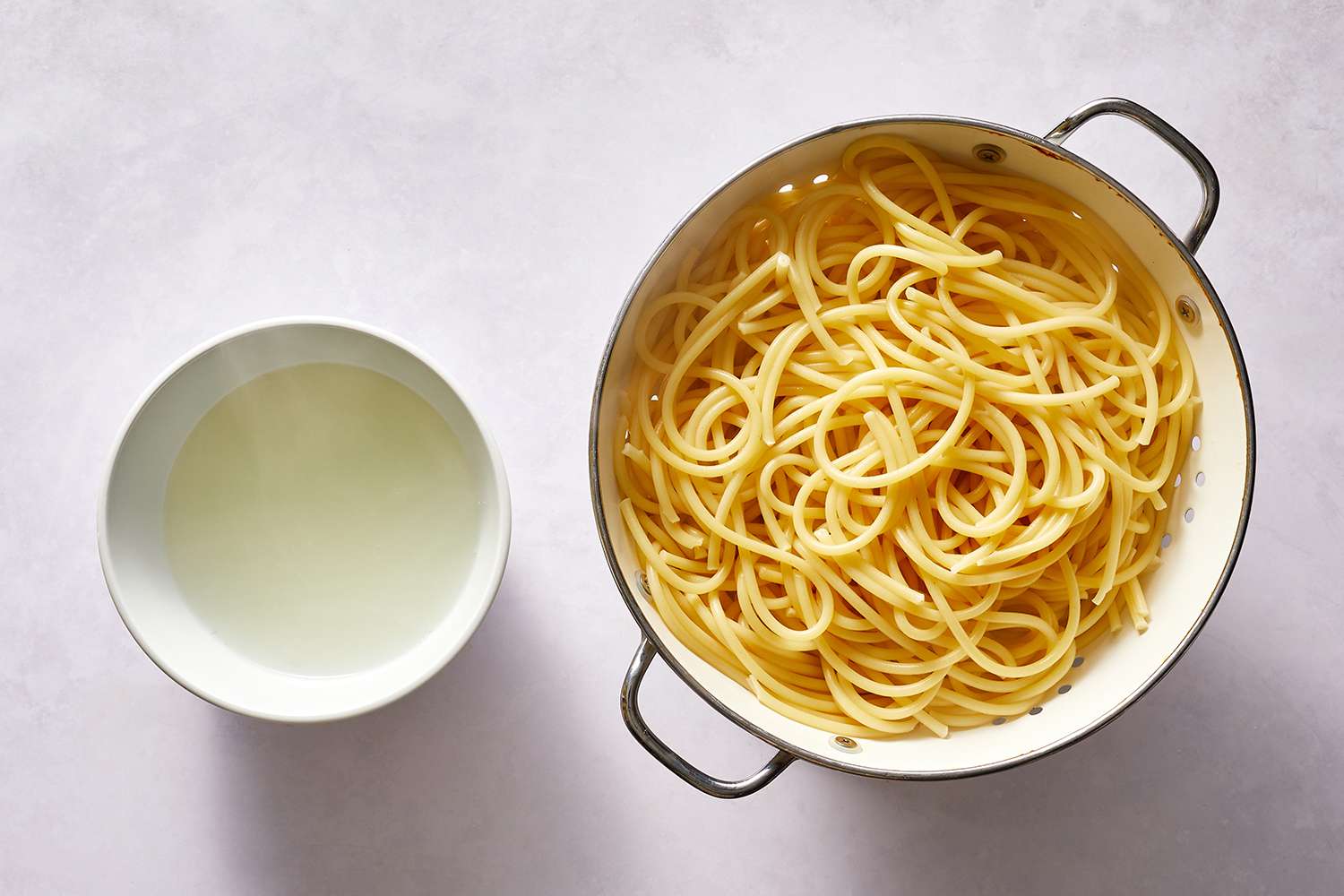 Cooked pasta drained in colander with reserved pasta water in a bowl