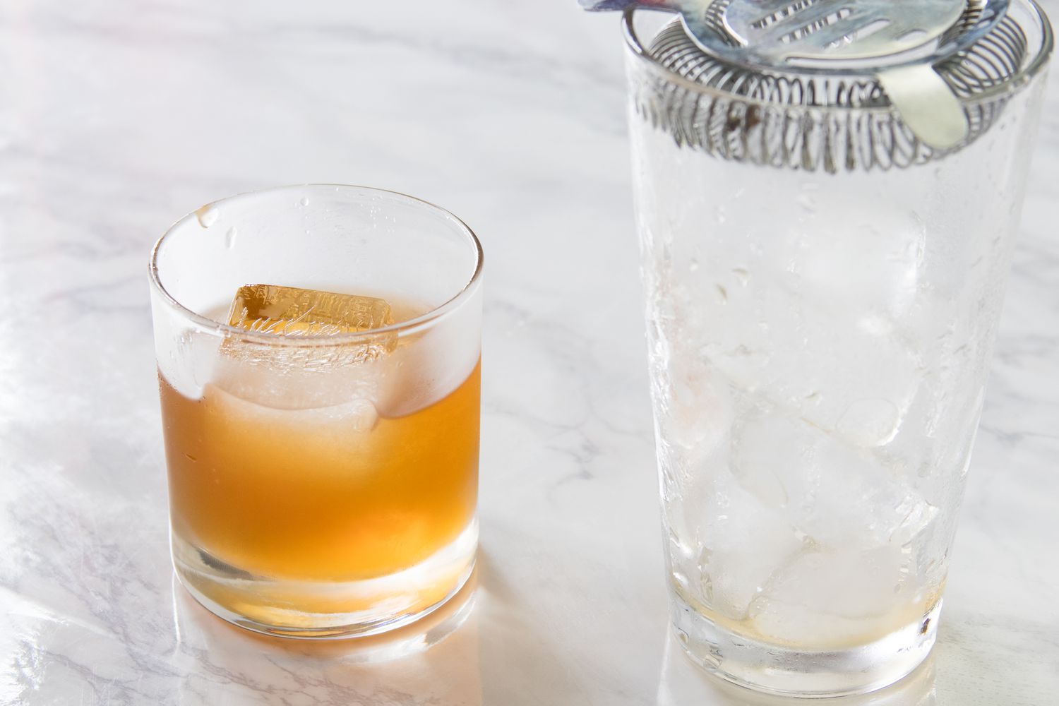 Amaretto sour strained into an old-fashioned glass next to a strainer over a glass with ice