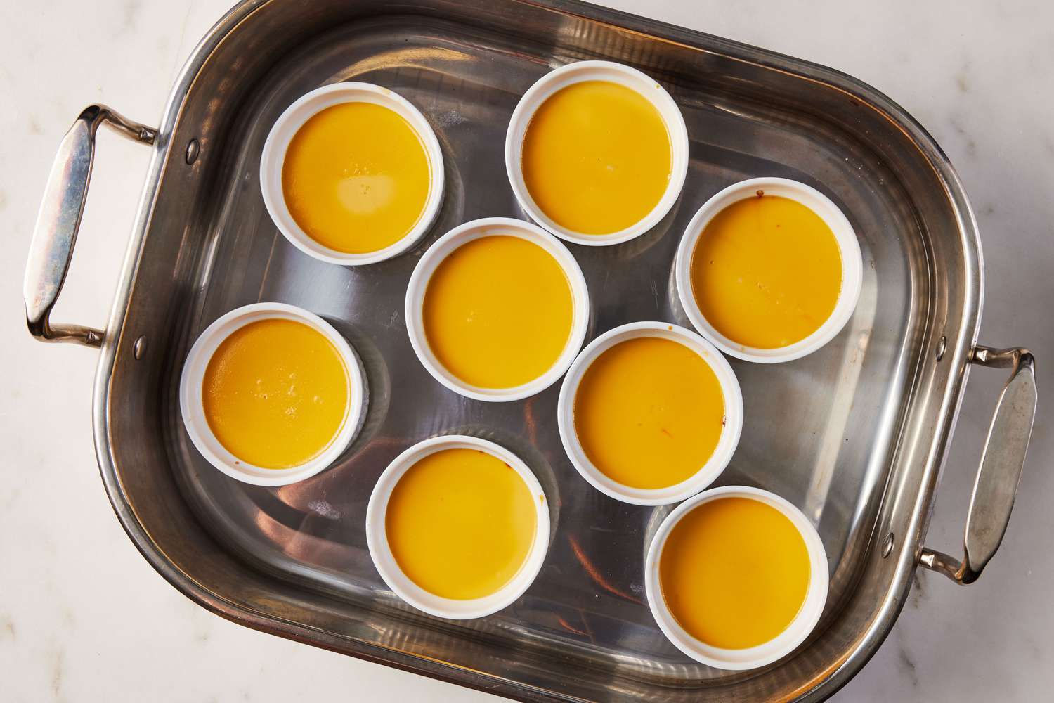 A roasting pan with eight cooked mango flans in small ramekins