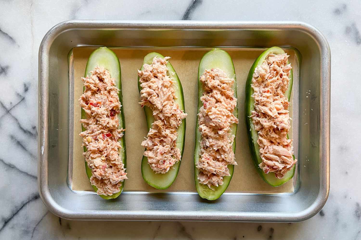 Halved cucumbers sitting on a small sheet pan with now-pink tuna filling stuffed inside