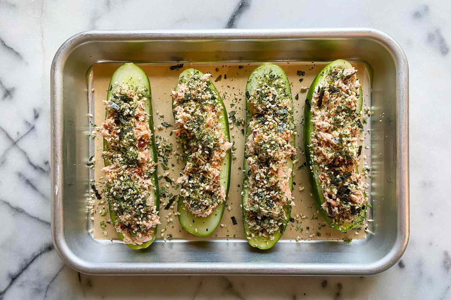 Overhead shot of halved cucumbers on a small sheet pan filled with tuna mixture and topped with furikake