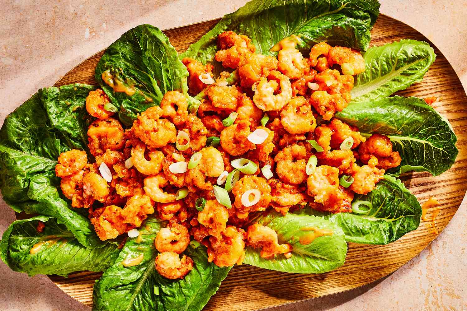 A platter of bang bang shrimp served on lettuce, topped with sliced scallions