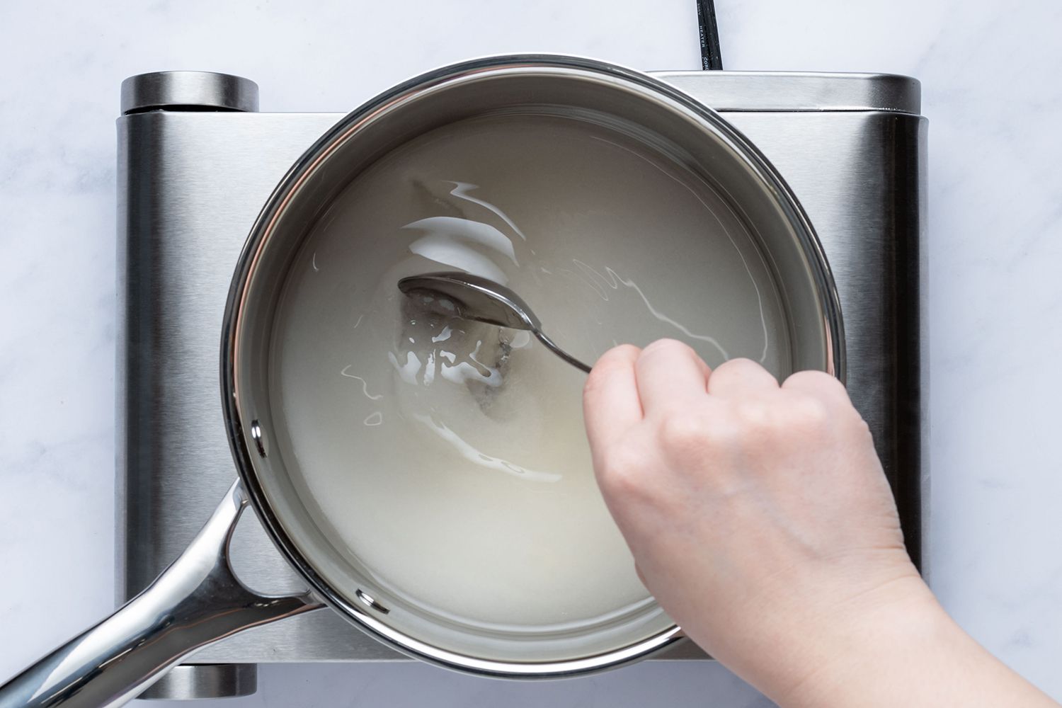 Stirring water and sugar mixture in the saucepan on the burner 