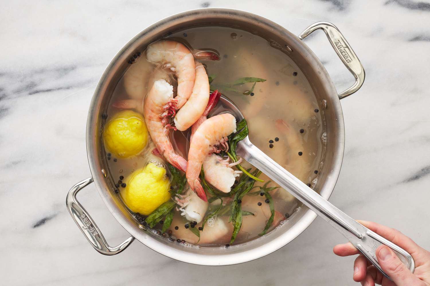 A large pot of seasoned water with lemon, thyme, and peppercorns with jumbo shrimp being lifted out with a giant metal spoon