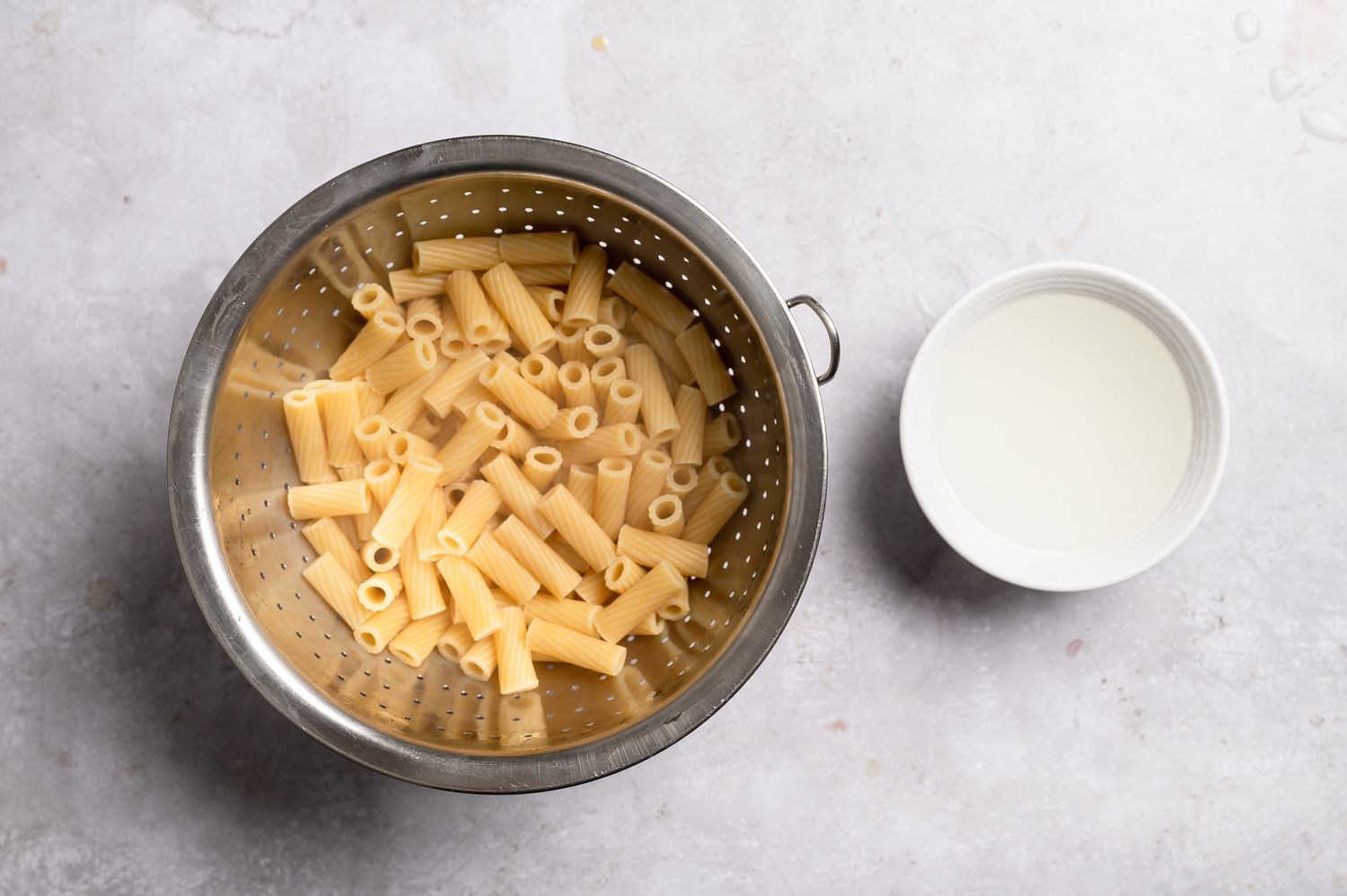 Cooked pasta in a colander with a small bowl of reserved pasta water