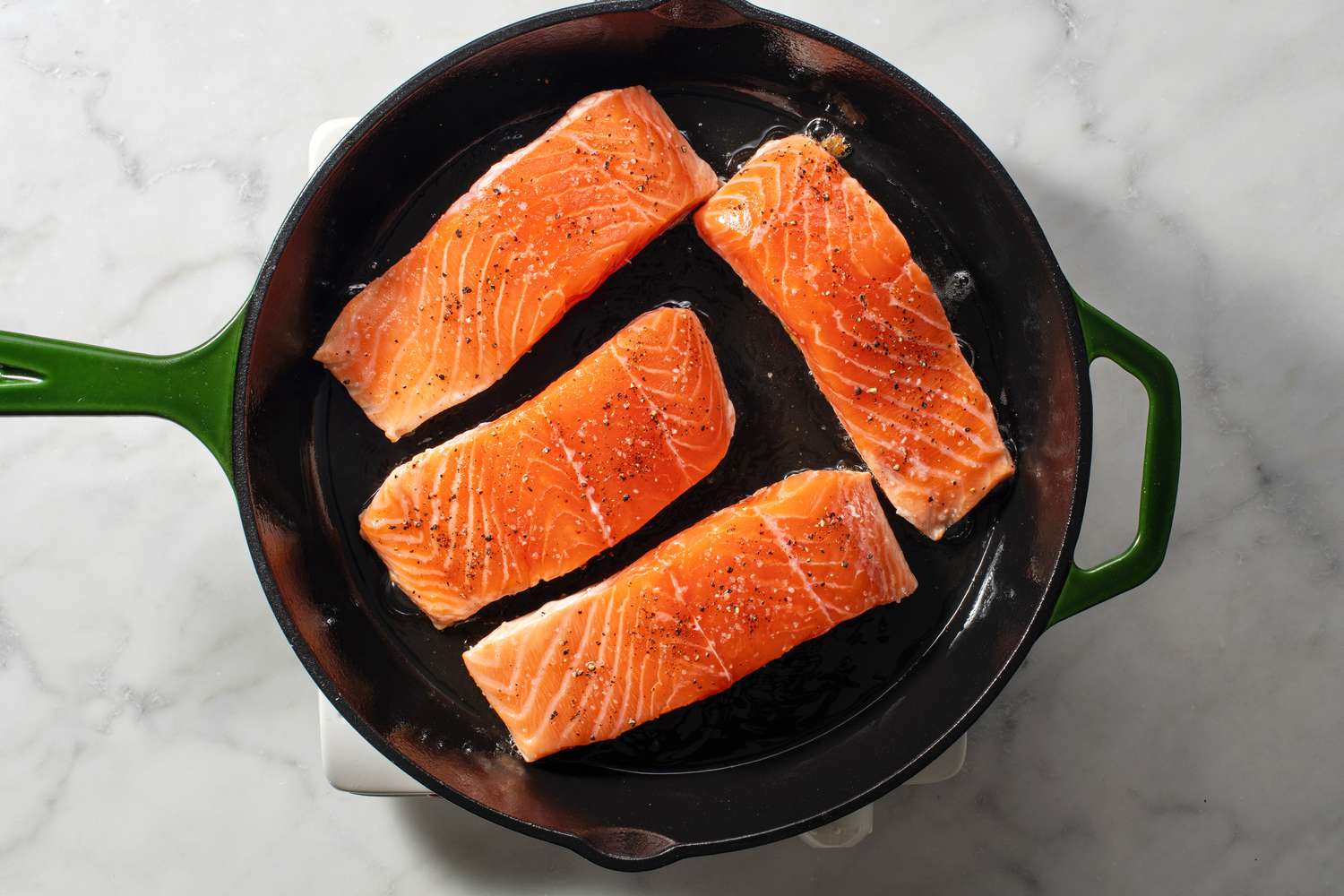 A skillet with four pieces of salmon, skin-side down