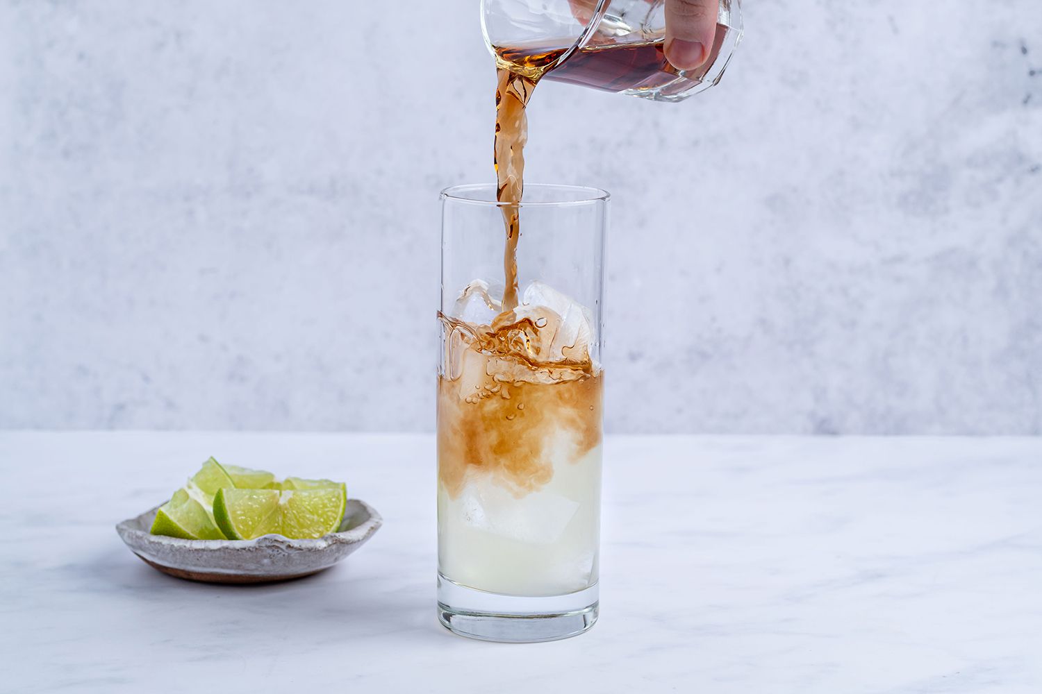 Dark Cane Spirit poured into a glass with Dark 'n Stormy Mocktail ingredients, and lime wedges in a bowl