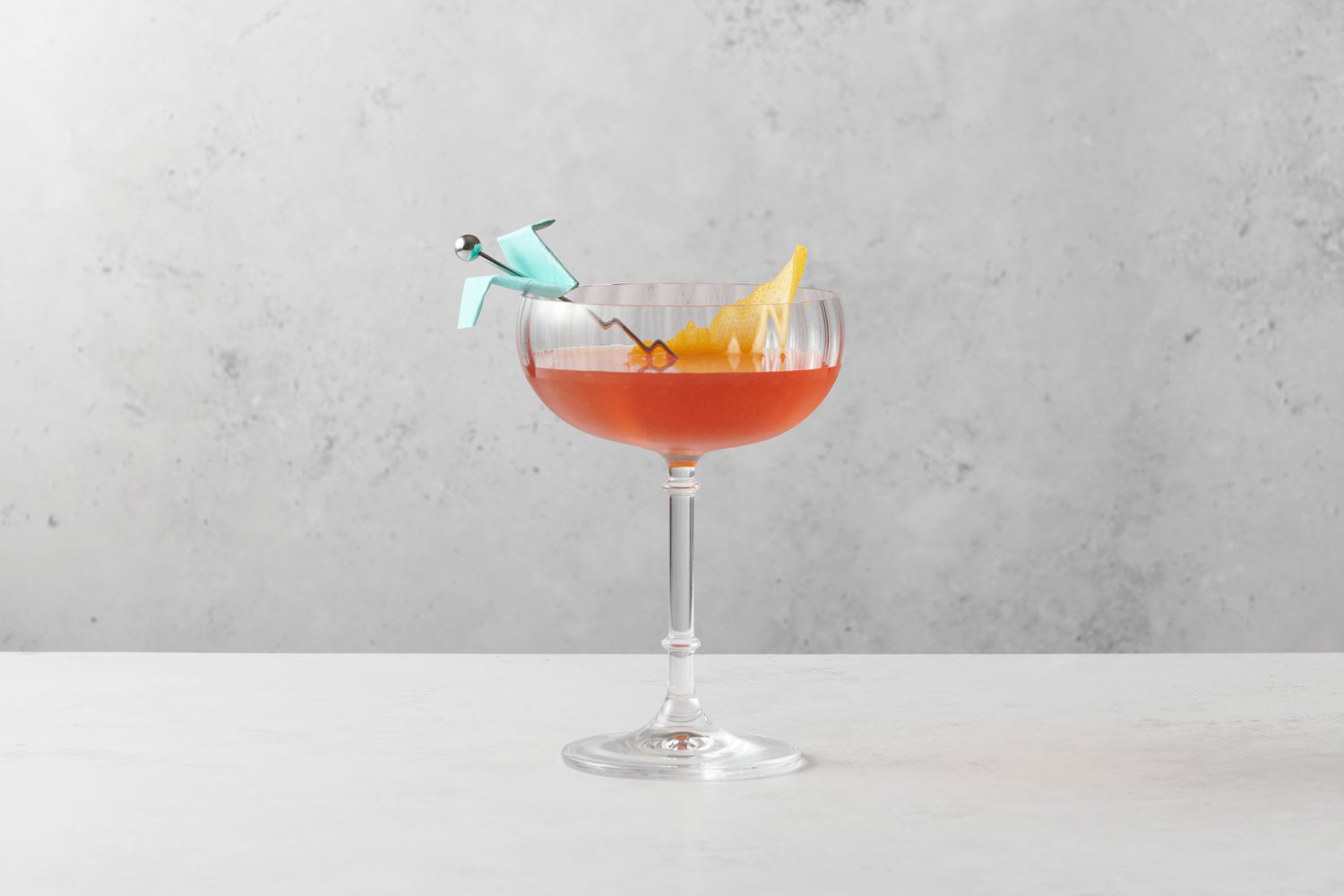 A Paper Plane cocktail garnished with a small paper plane and a lemon peel