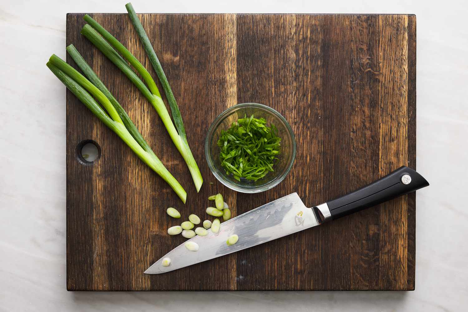 scallions on cutting board being sliced with chef knife