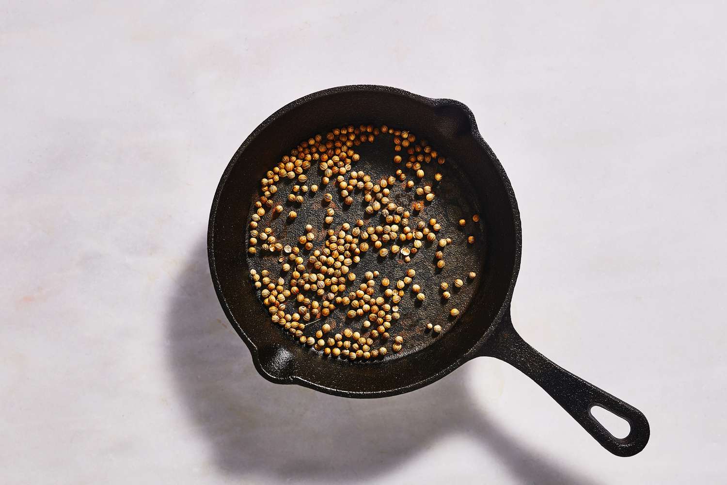 A small cast iron skillet with toasted coriander seeds