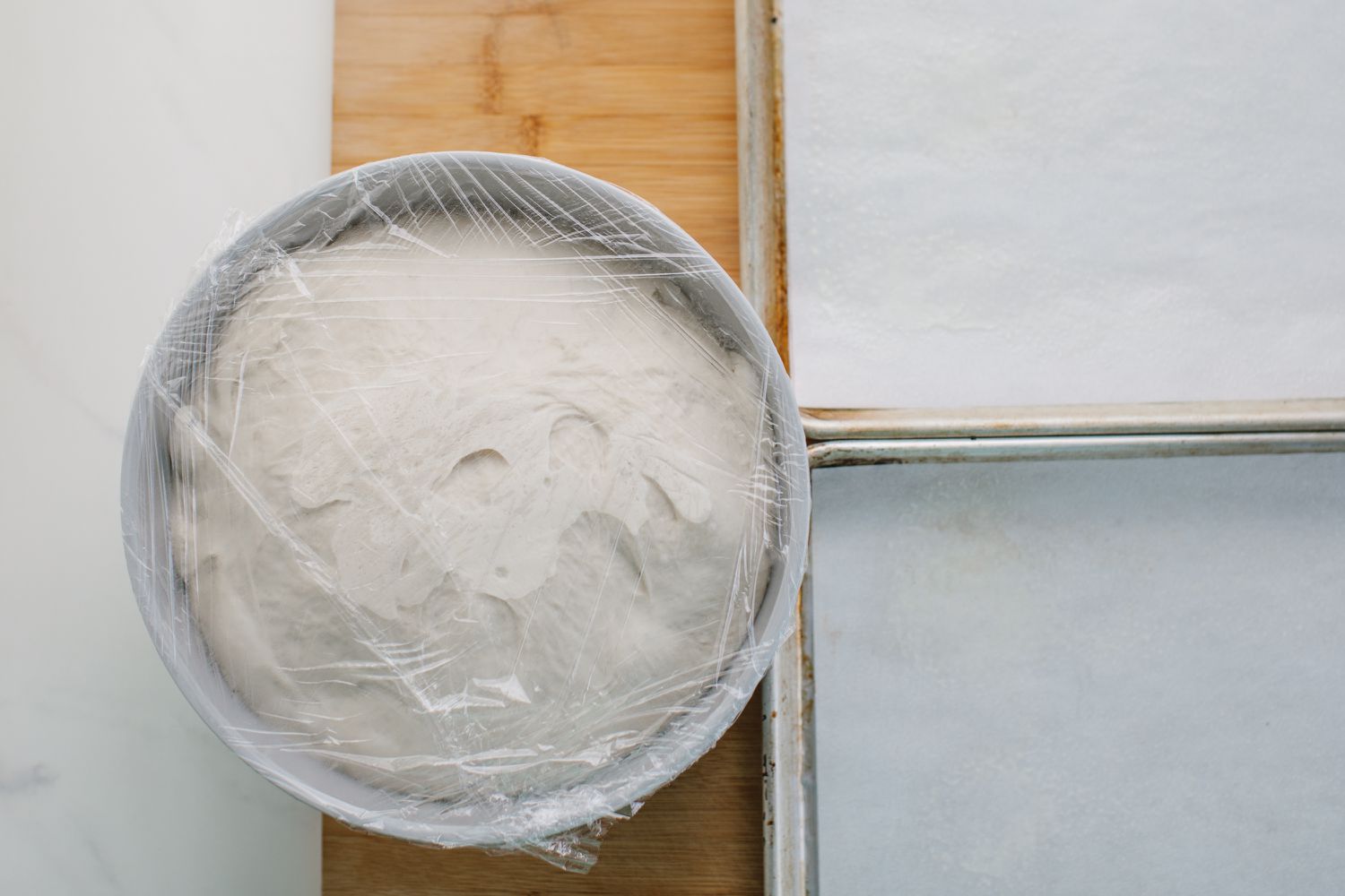 Dough covered in plastic wrap next to baking sheets
