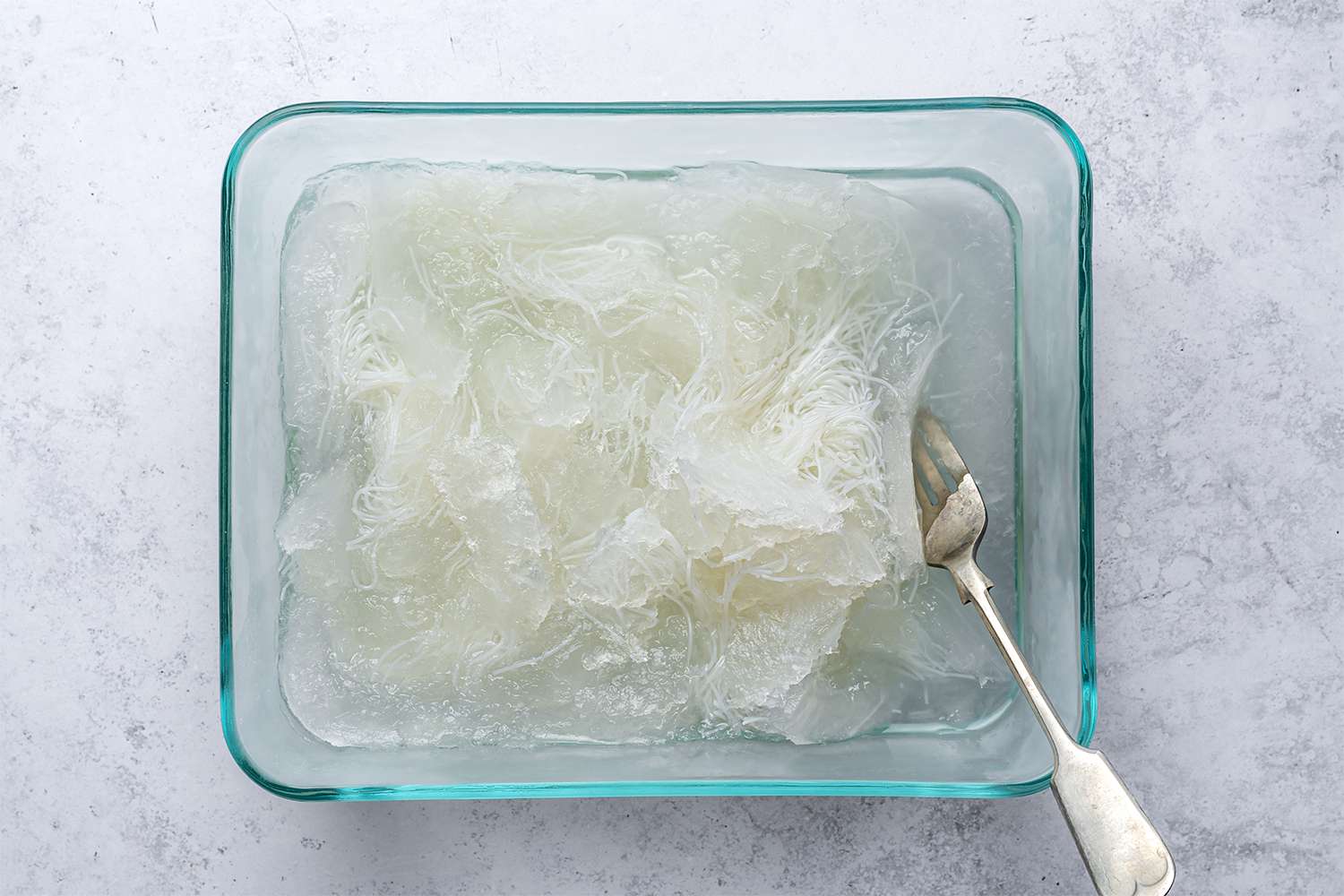 Frozen syrup and rice noodle mixture in a baking dish, with a spoon 