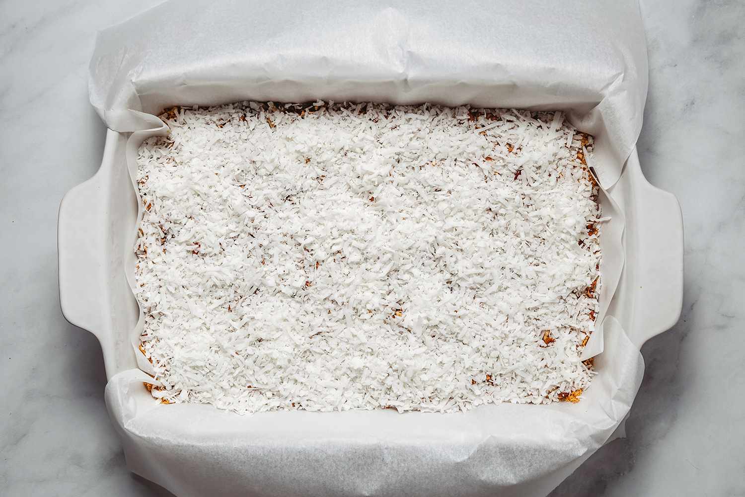 Coconut flakes on top of the chocolate and nut mixture in the prepared baking pan