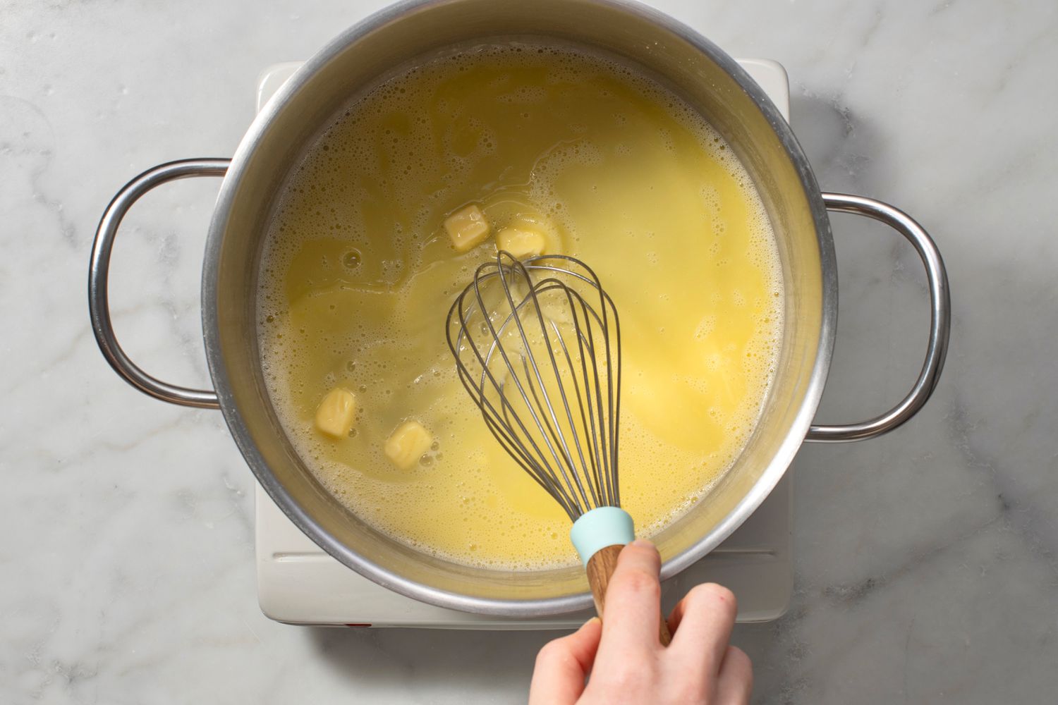 A hand whisking butter and pasta water in a large pot
