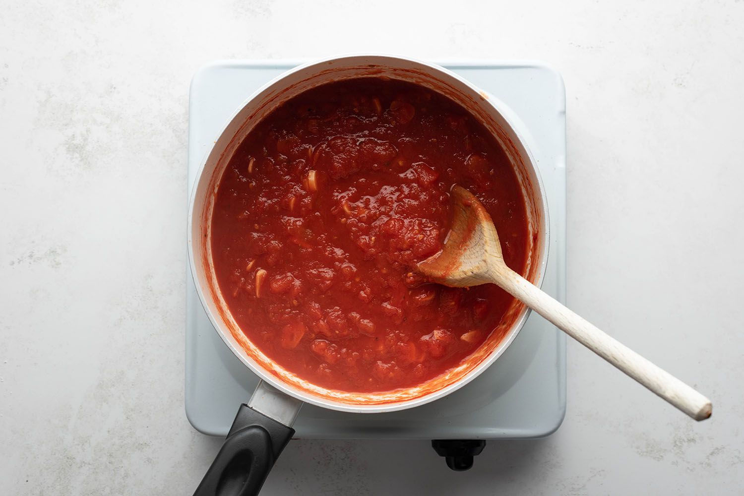 Marinara sauce cooking in a pot on a burner, with a wooden spoon 