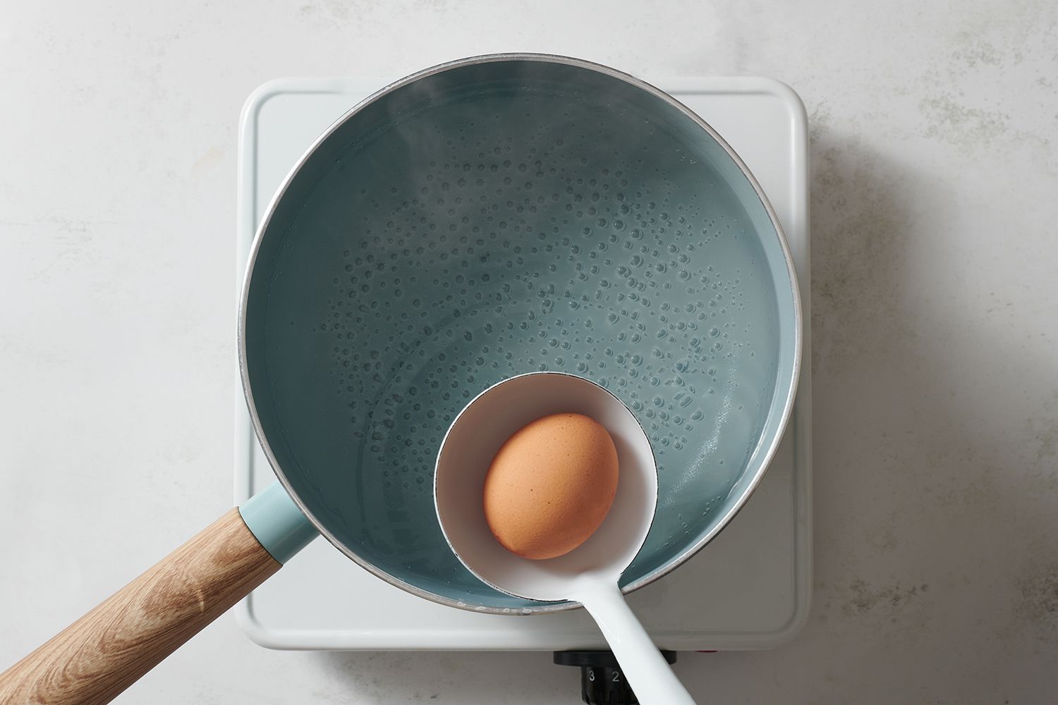 A ladle adding an egg to a pot of hot water