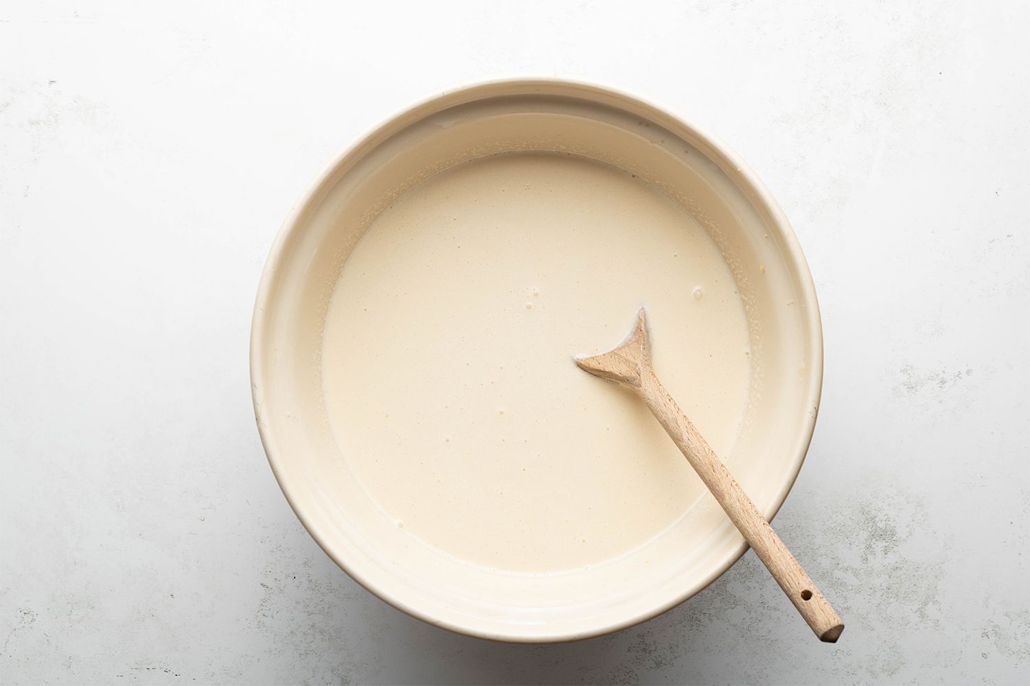 Milk, heavy cream, whiskey, and vanilla mixture in a bowl with a wooden spoon