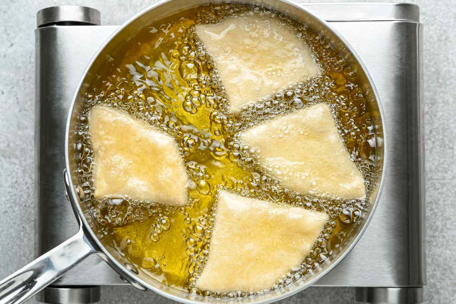 Four wedges of dough frying in a large pot of oil