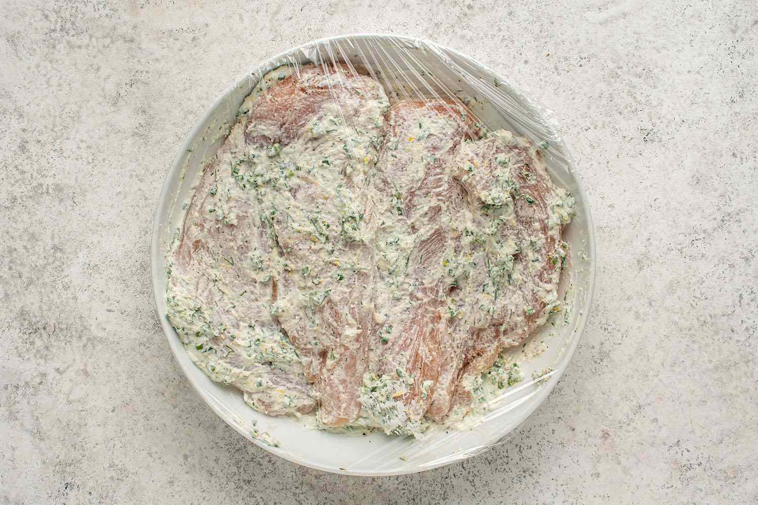 Chicken with sour cream in a bowl, covered with plastic wrap 
