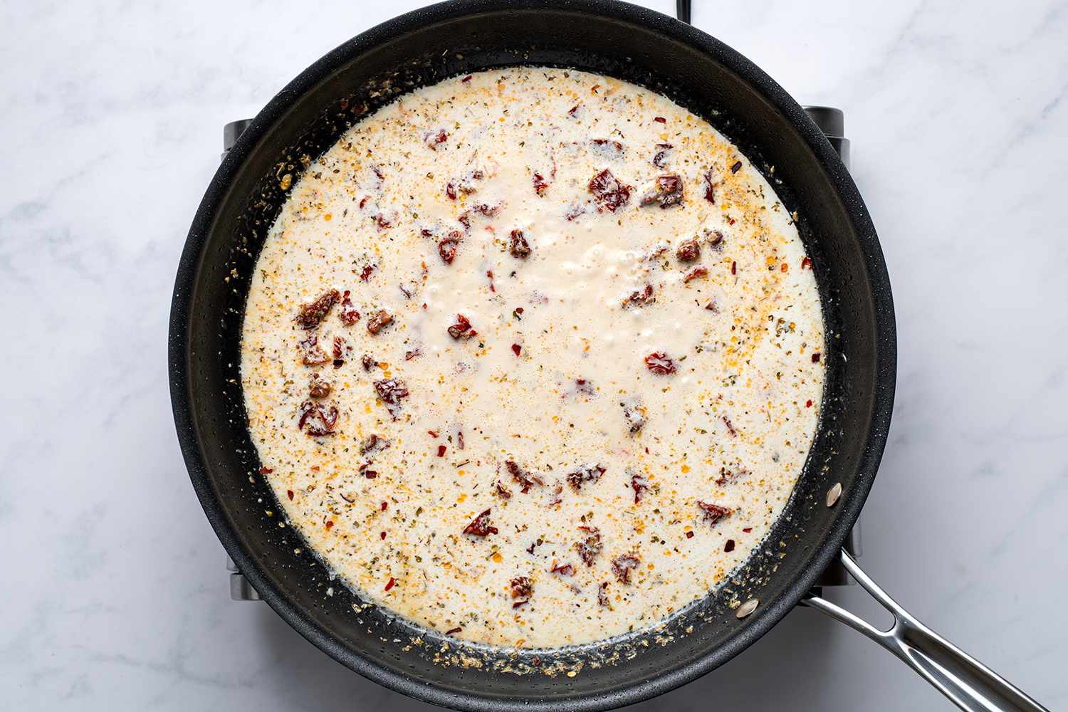 Creamy sauce with bits of sun-dried tomatoes simmering in a skillet