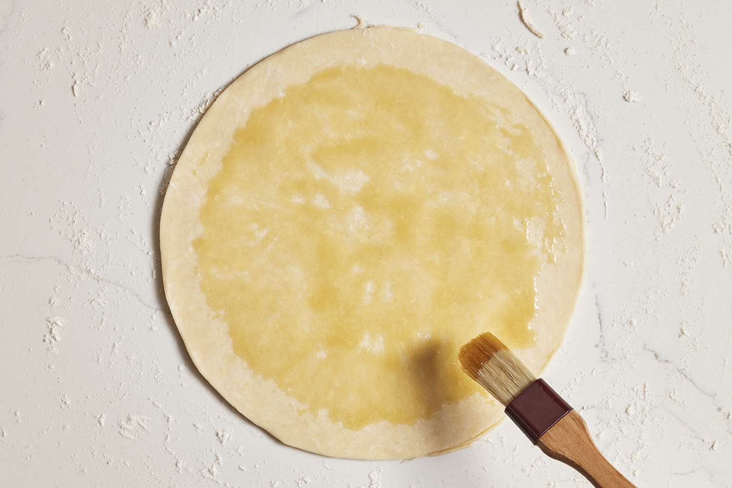 honey being applied to dough round with pastry brush