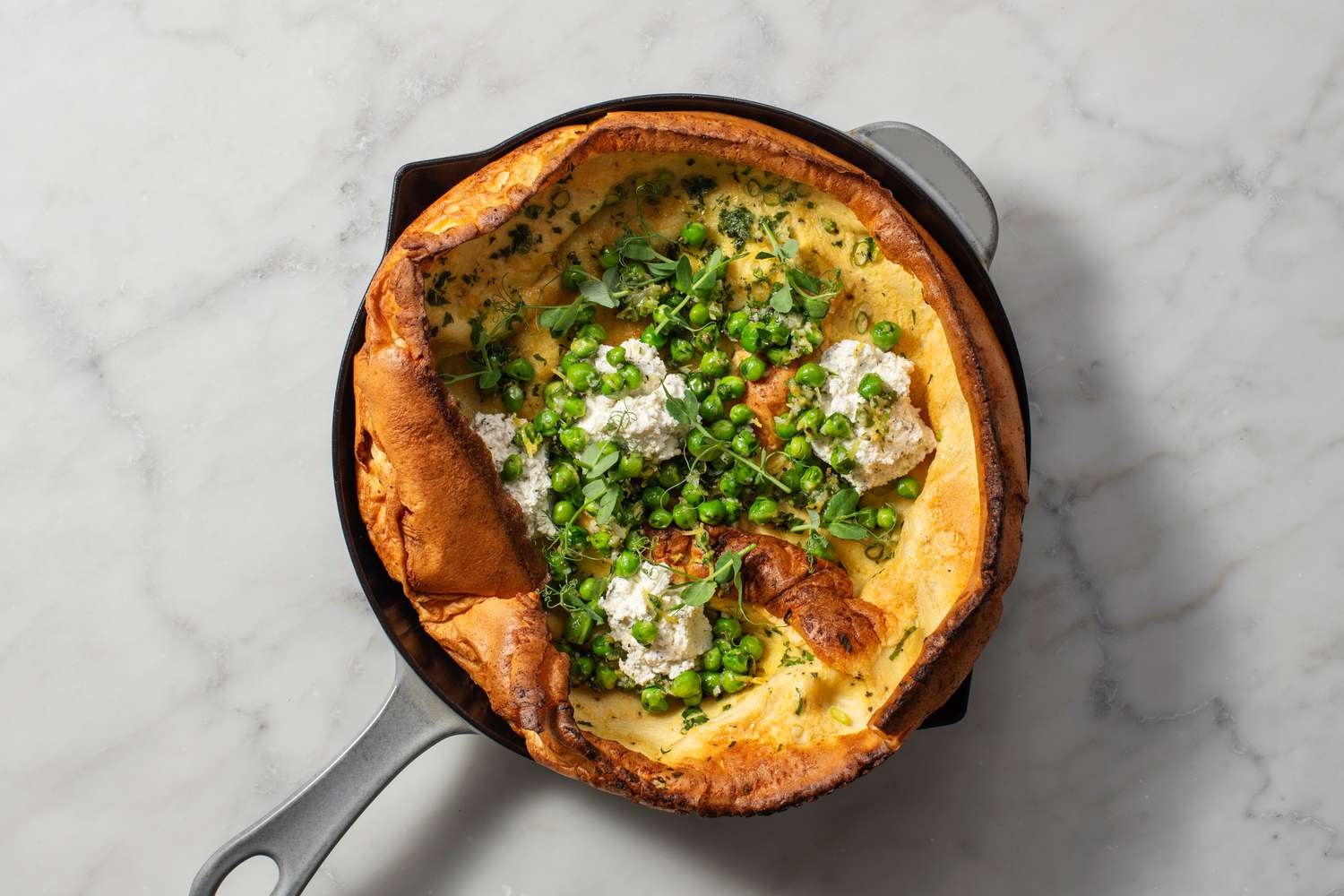 A Boursin and peas Dutch Baby garnished with parsley and pea shoots
