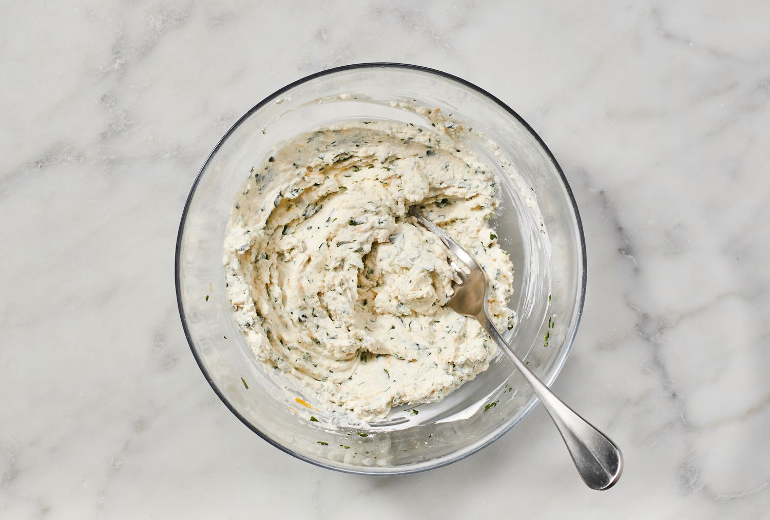 A bowl of combined cream cheese, Parmigiano Reggiano, garlic, basil, parsley, lemon zest, and salt