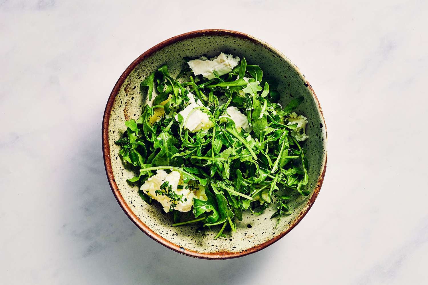 A bowl of arugula, chevre cheese, lemon juice, parsley, and chives