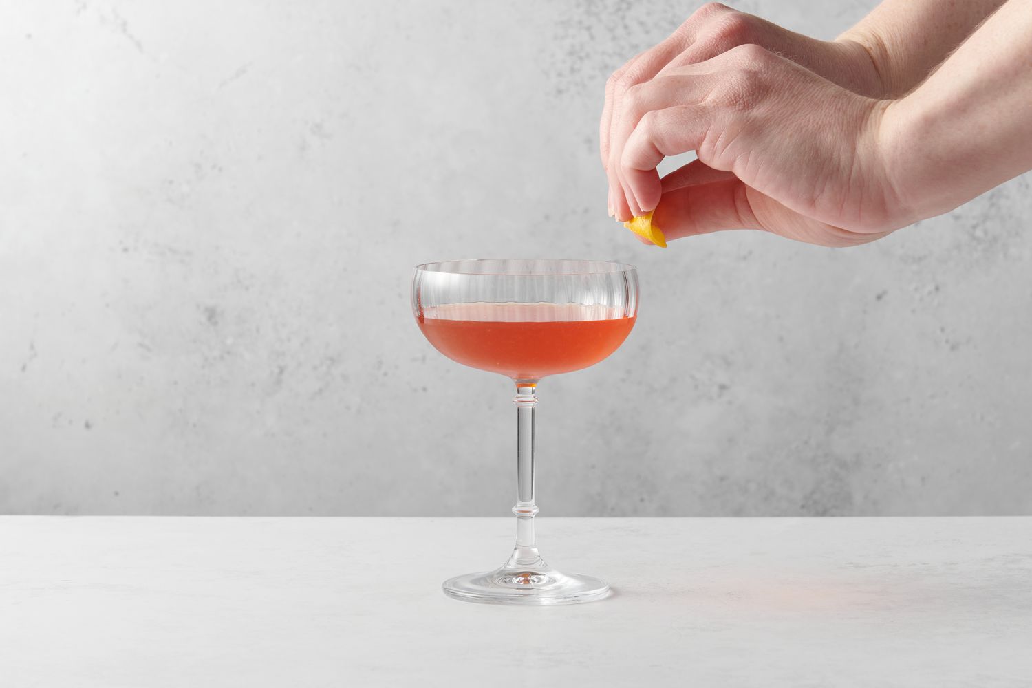 A hand expressing a lemon peel into a cocktail