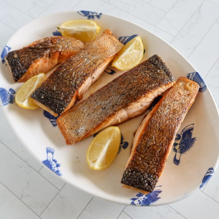 Four browned salmon fillets on a serving platter with lemon wedges