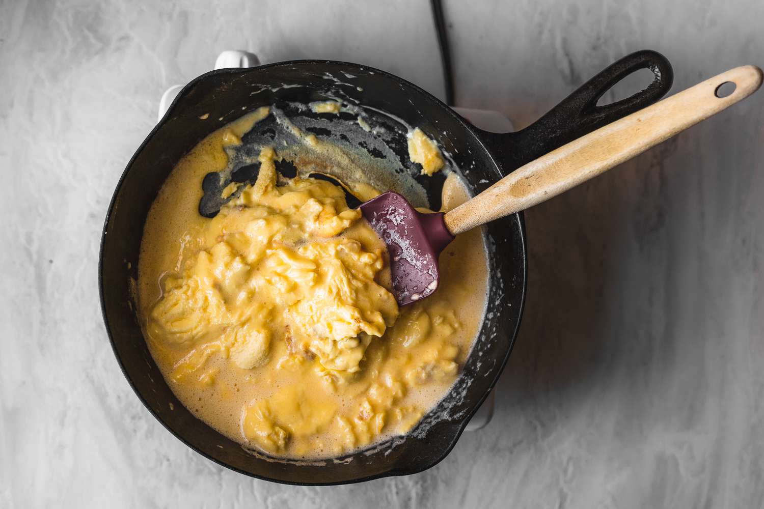 Scrambled eggs in a cast-iron skillet being stirred with a rubber spatula