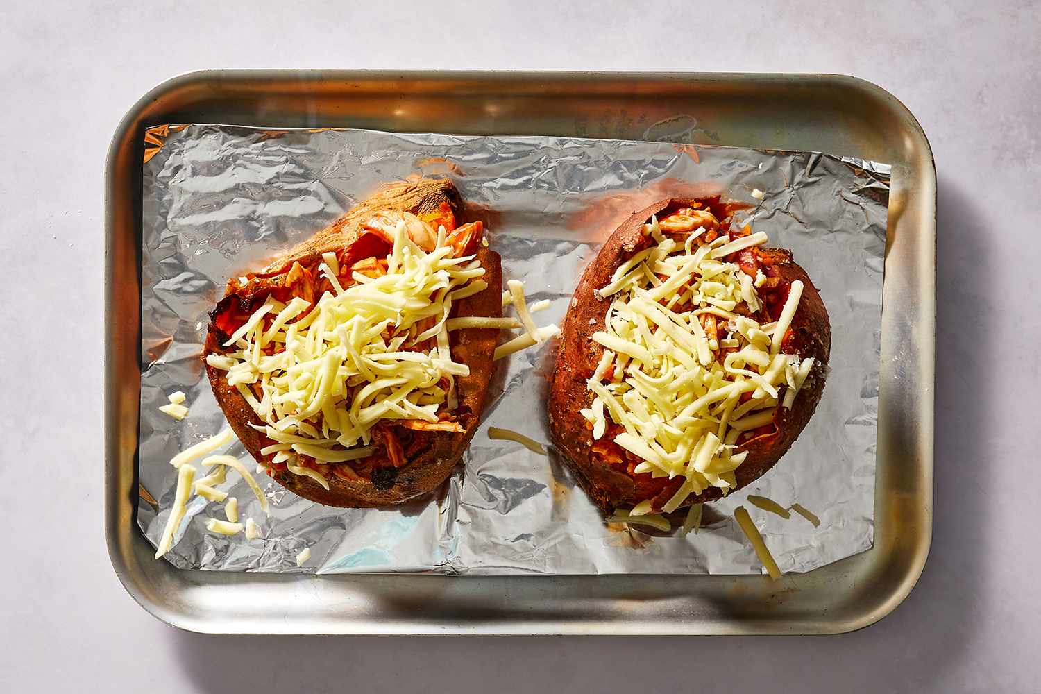 BBQ Chicken Stuffed Sweet Potatoes topped with cheese on a baking sheet 