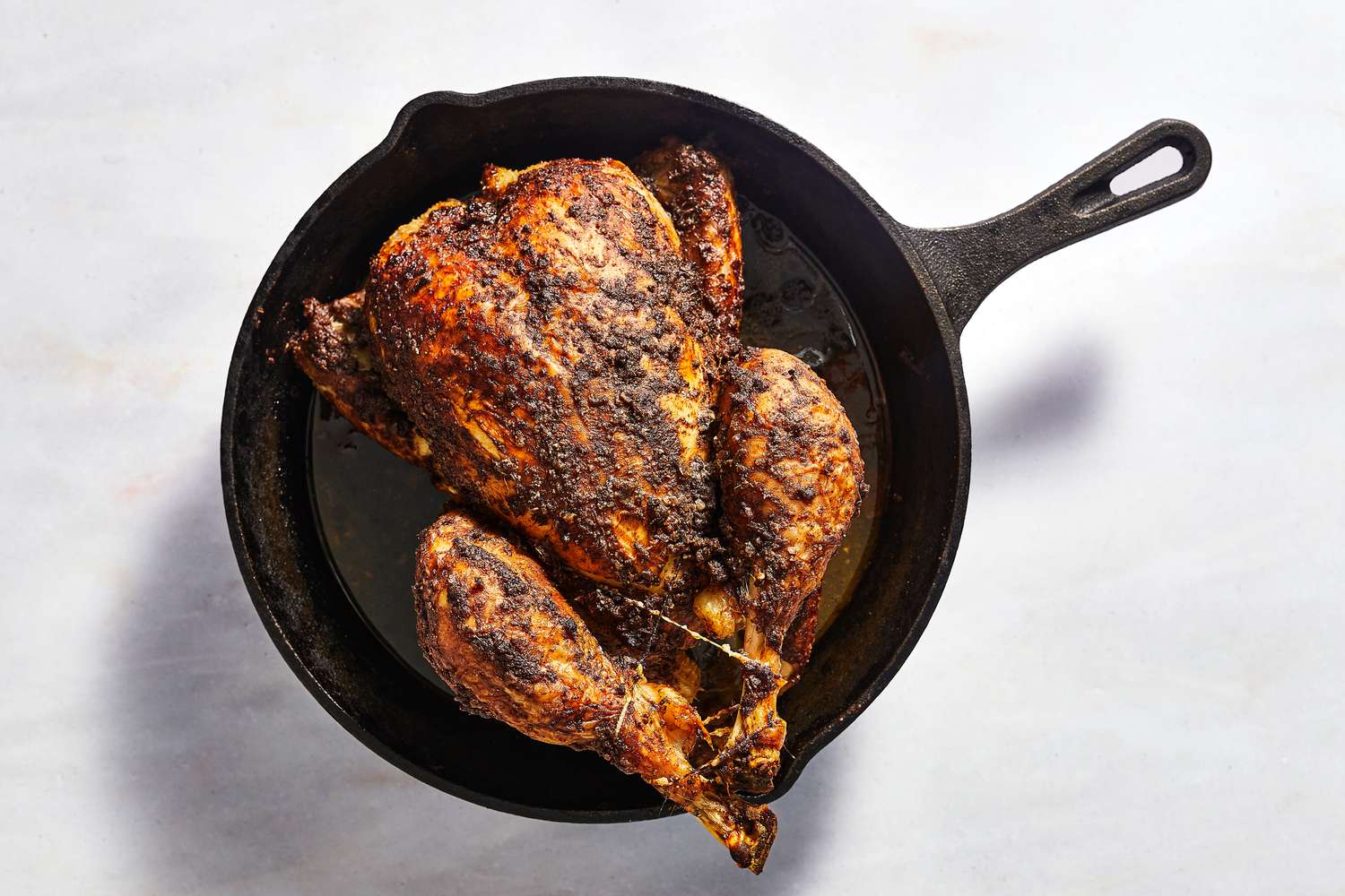 A whole roasted chicken, coated with oil-spice mixture, trussed, in a cast iron skillet