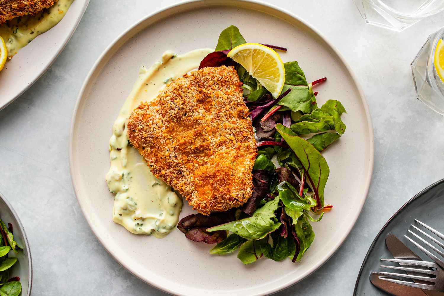 Panko-crusted oven-fried haddock on a plate with mixed greens, tartar sauce, and sliced orange